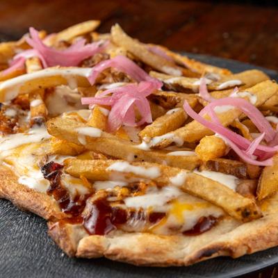 Pittsburgher flatbread with chicken, bacon, fries, cheese, and BBQ sauce.