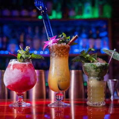 Three tropical cocktails lined up on a bar counter.