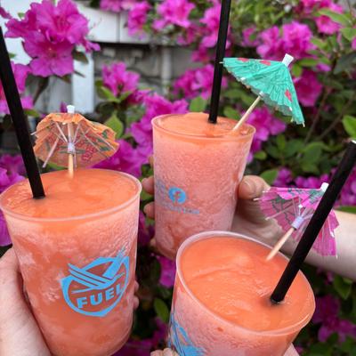 Toasting with three orange slush drinks, held up against a backdrop of purple flowers.