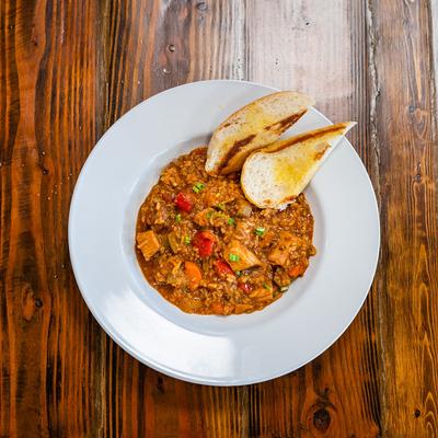 Hearty stew with colorful vegetables and diced meat on a white plate with toasted bread slices.