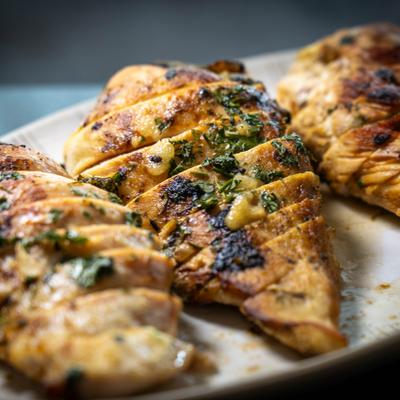 Sliced grilled chicken with herbs on plate.