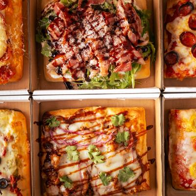 Six square deep-dish pizzas with meats, drizzles, and greens in boxes.