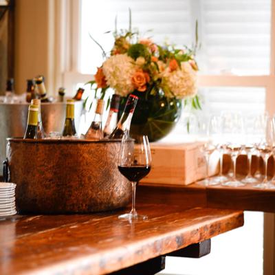 Bottles in a  bucket with a glass of red wine and flowers by a window.