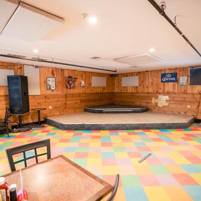 Restaurant interior with wood-paneled walls, colorful tiled floor, and a small empty stage.