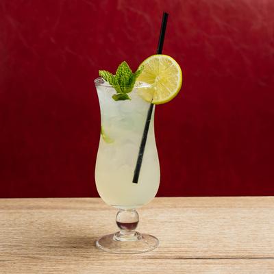 A glass of mojito  sits on a wooden table against a red background.