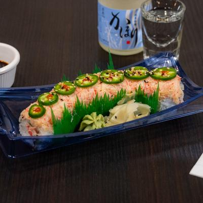 Sushi roll topped with sliced jalapenos and sesame seeds, alongside glass of sake.