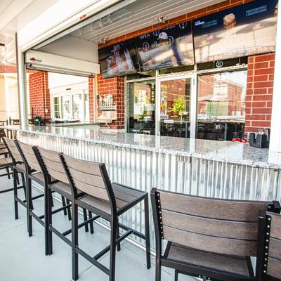 Outdoor bar with a marble counter, stools, and TVs.
