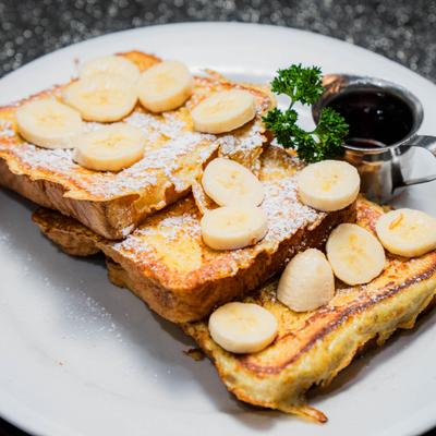 French toast topped with banana slices and powdered sugar, served with syrup.