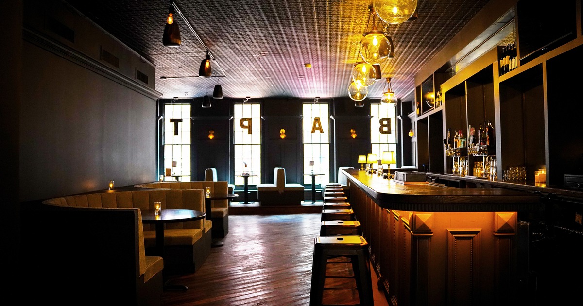 Stylish bar interior with a long bar counter with stools and booth-style seating with round tables