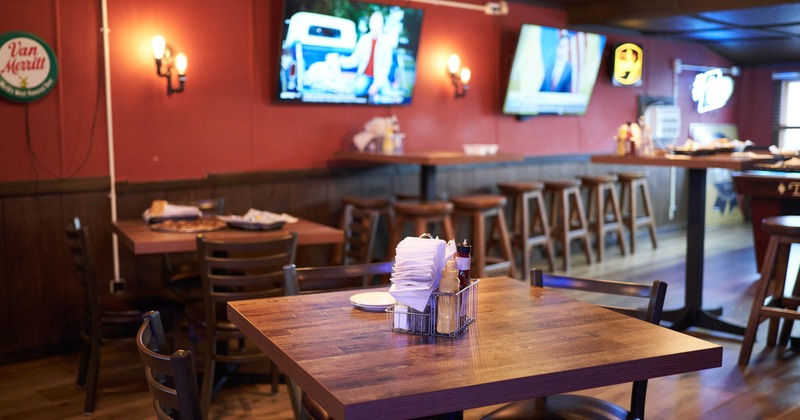 Interior of a bar with wooden tables and chairs, red walls, and two TV's