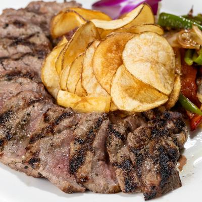 Black Angus Boneless Shell Steak with chips and cooked vegetables, close up.