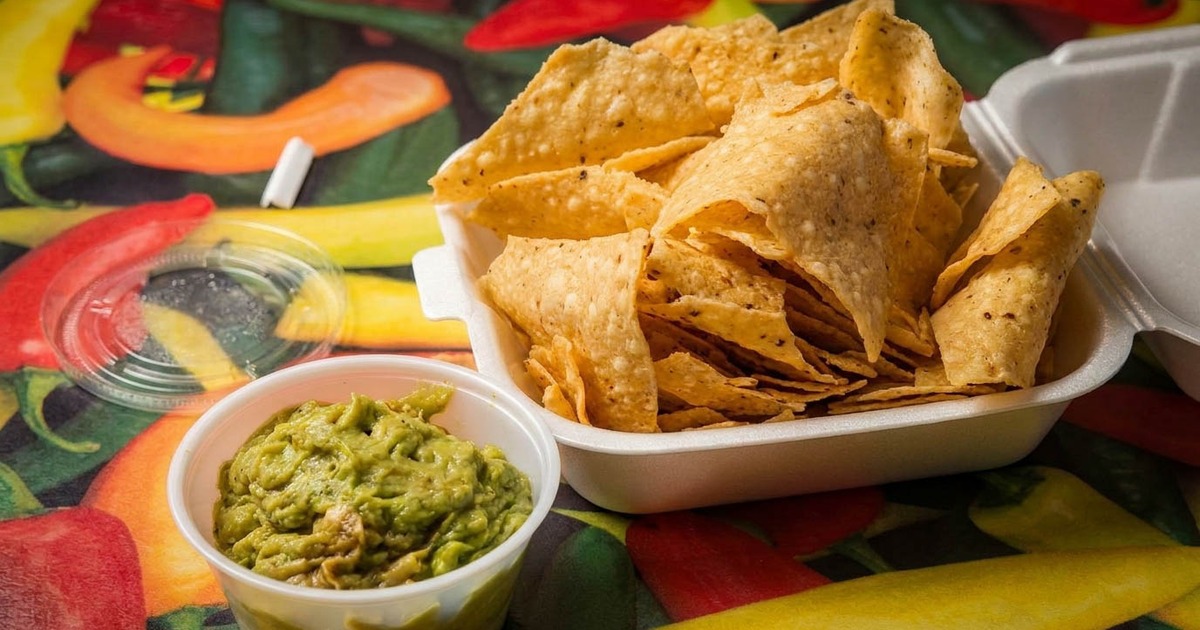 Tortilla chips in a takeout container next to green guacamole