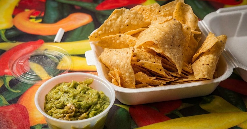 Tortilla chips in a takeout container next to green guacamole