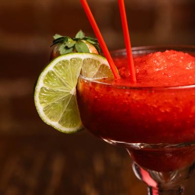 Cocktail served in Margarita glass, garnished with lime wheel and a strawberry.