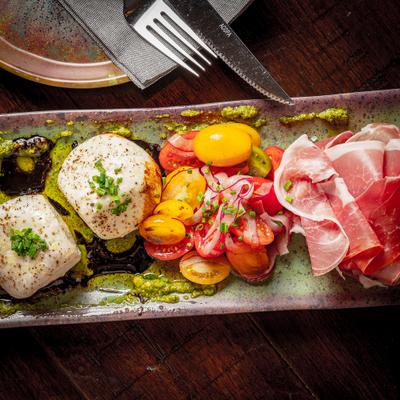 Burrata and prosciutto board with tomatoes and pesto.