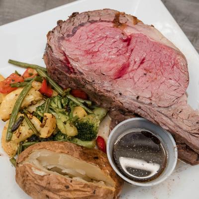 Roast beef accompanied by a side of au jus, baked potato and sautéed vegetables.