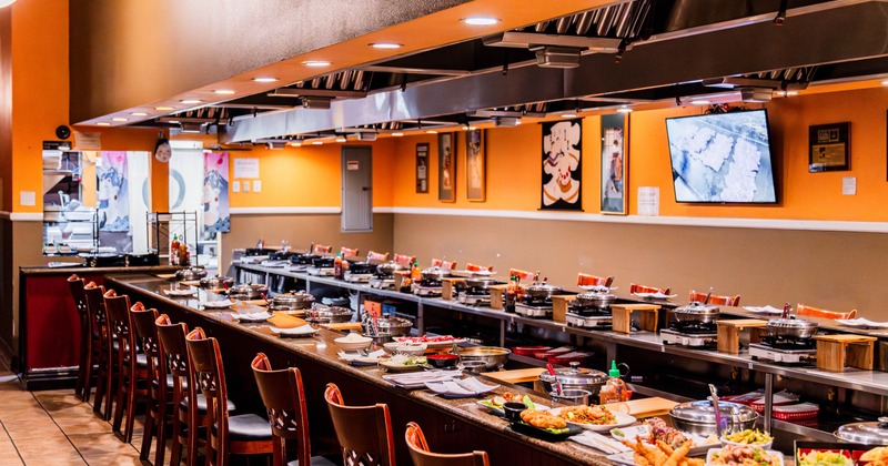 Interior of a restaurant with a long counter featuring cooking setups and wooden chairs