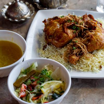 Roasted chicken served over rice with a salad and a bowl of soup on the side.