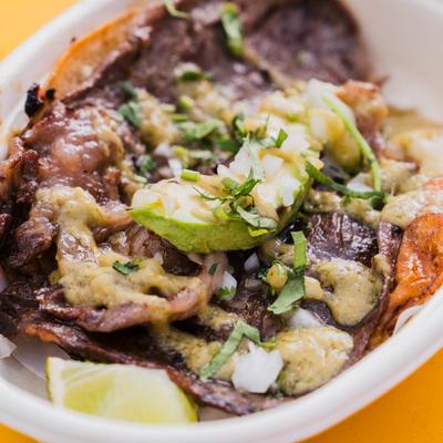 Bistec taco topped with salsa verde, avocado, onions, and cilantro.