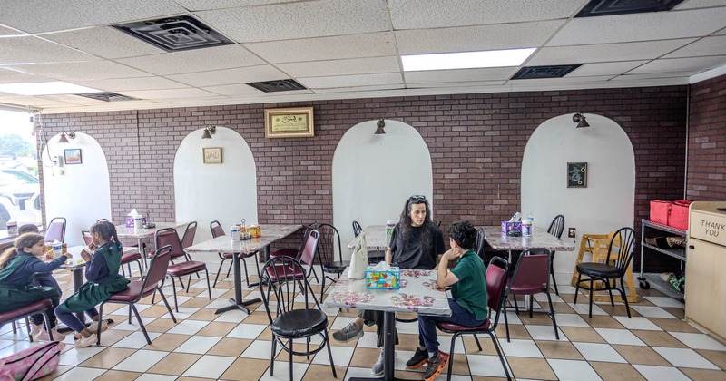 A few guests sitting in a casual seating area with checkered flooring and brick walls
