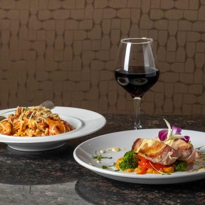 Two plates of elegant food served alongside a red wine.