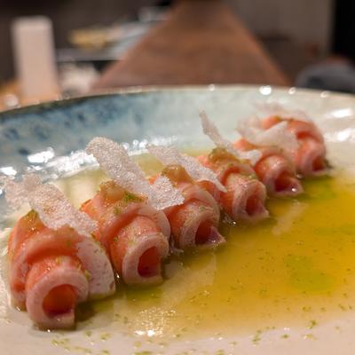Rolled raw salmon slices plated in olive oil with crispy garnish.