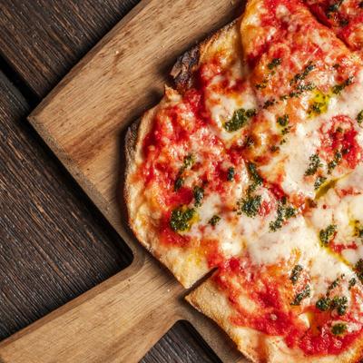 Pinsa Margherita served on a wooden cutting board, close-up.