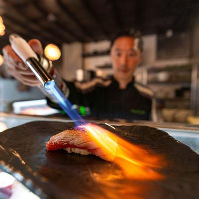 Chef grilling a nigiri with a butane torch.