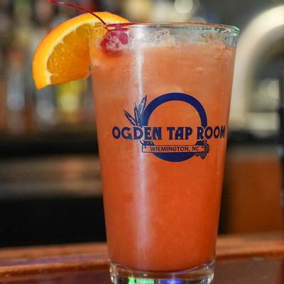 Red Berry Crush served in a branded pint glass, garnished with a cheery and a slice of orange.