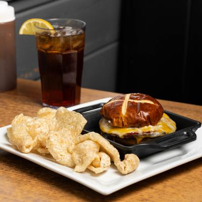 Bologna Sandwich served with pork rinds, alongside glass of iced drink.