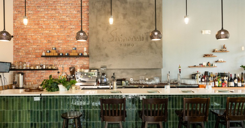 Modern bar interior with rustic brick and gray walls, wooden stools, and a green tile counter