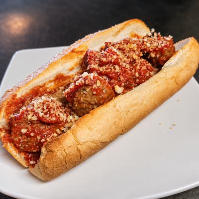 A meatball sub with tomato sauce and grated cheese on a white plate..