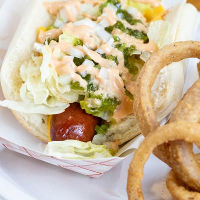 Pickled hot dog topped with onions amd lettuce, served with onion rings.
