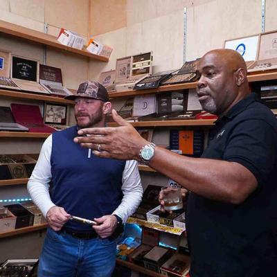 Two people surrounded by various cigar boxes and accessories.