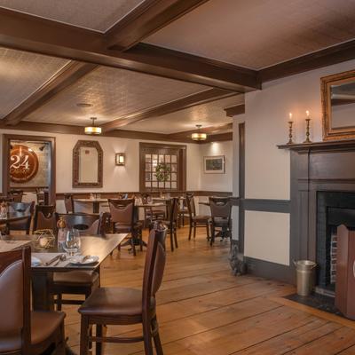 Interior, wooden floors and classic decor, tables are set with glassware, a lit fireplace.