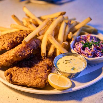 Crispy fried fish fillets with fries, coleslaw, and dipping sauce.