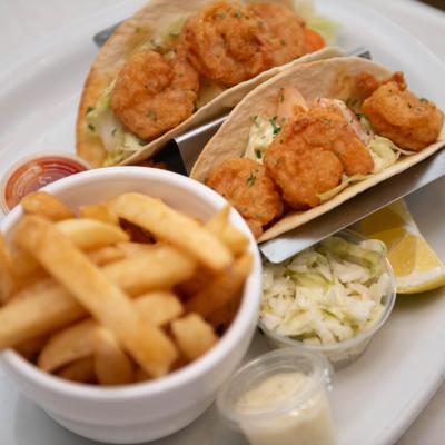 Fish tacos served alongside fries, coleslaw and dipping sauces.