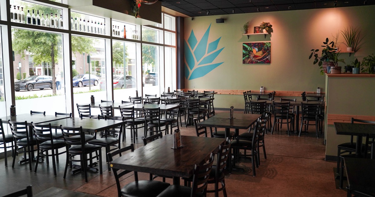 Dining area features wooden tables, dark chairs, and agave wall art
