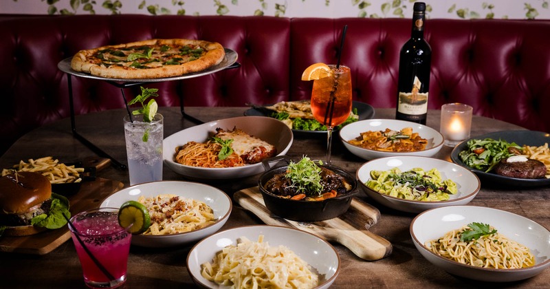A table filled with various dishes, cocktails and a wine bottle