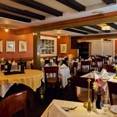 A warm restaurant dining room features several round tables set with white tablecloths.