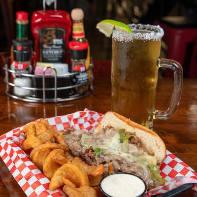 Philly cheese steak with fries and a sauce, accompanied with a mug of beer.