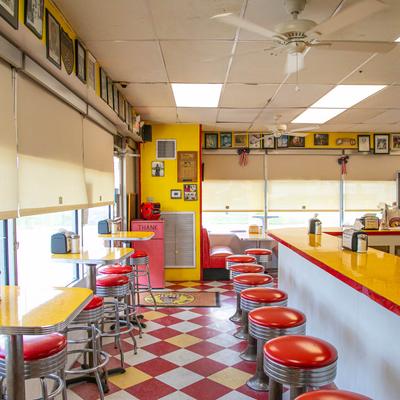 Retro diner interior with yellow checkered floor, red and chrome stools, and yellow countertops.