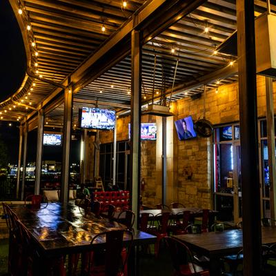Covered patio area with tables, chairs, string lights and television screens.