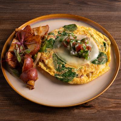 Omelet filled with spinach and cheese, topped with salsa, served with roasted potatoes.
