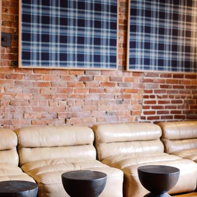 Lounge area with tan leather sofas against a brick wall with plaid artwork.