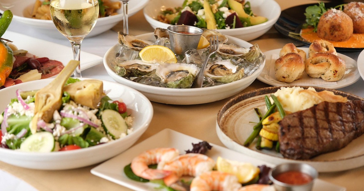 Large table spread with wine, seafood, steak, and salad plates