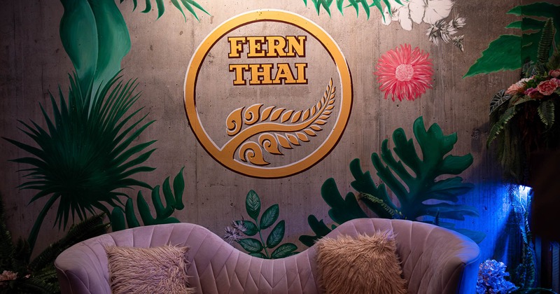 Interior, lounge sofa in front of a wall with plant mural and Fern Thai logomark