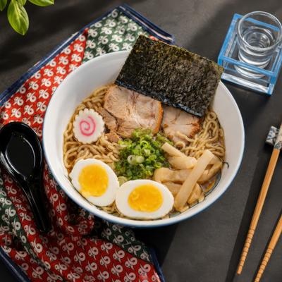 A bowl of ramen with eggs, pork, nori, and green onions.