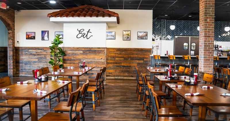 Interior seating area with wooden tables and chairs, a brick column and a bar area