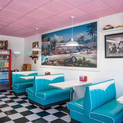 Interior of a retro diner with turquoise booths, checkered flooring, and a pink ceiling.